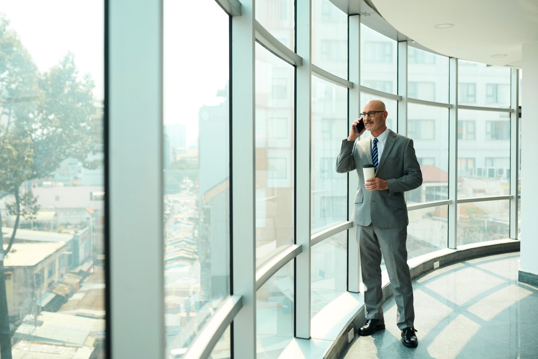 Businessman holding coffee while talking on phone in modern office