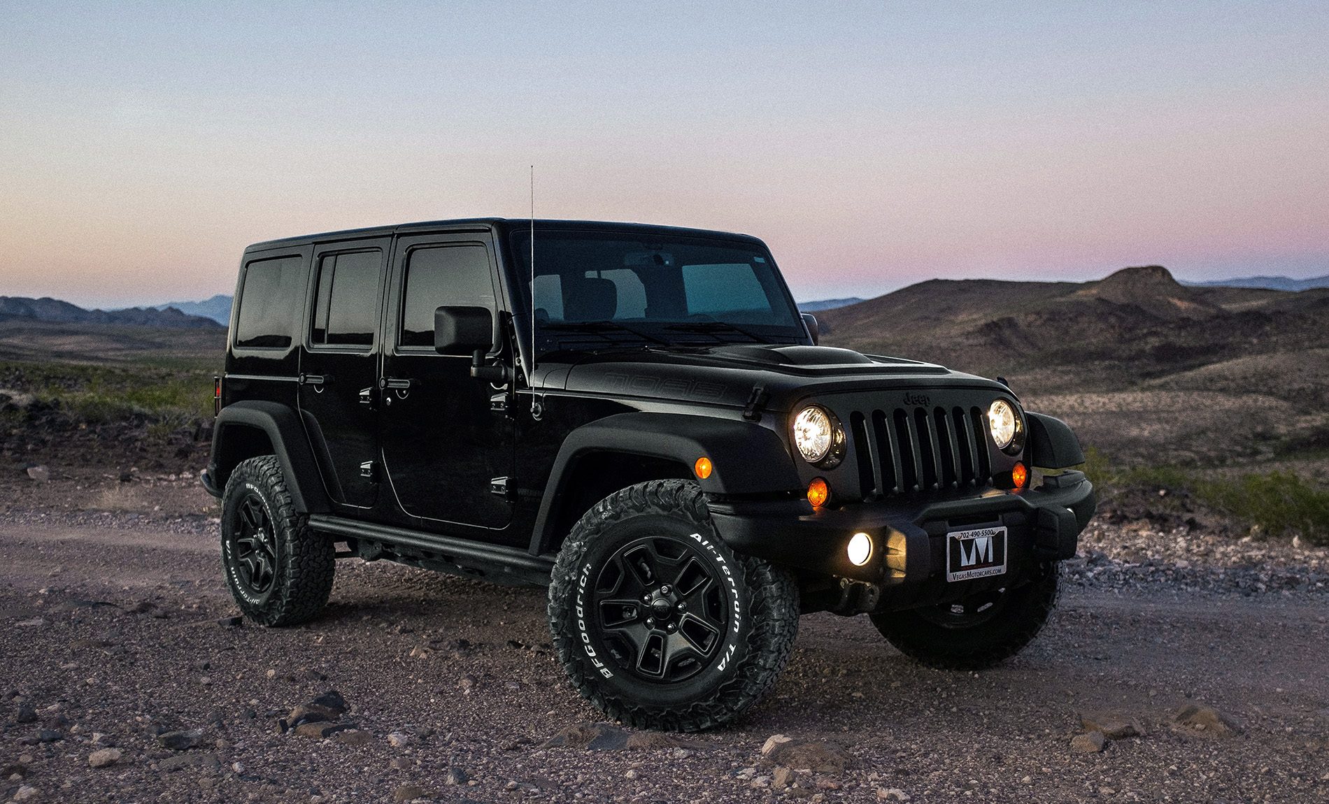 Black Jeep Wrangler Unlimited parked on a desert trail at dusk