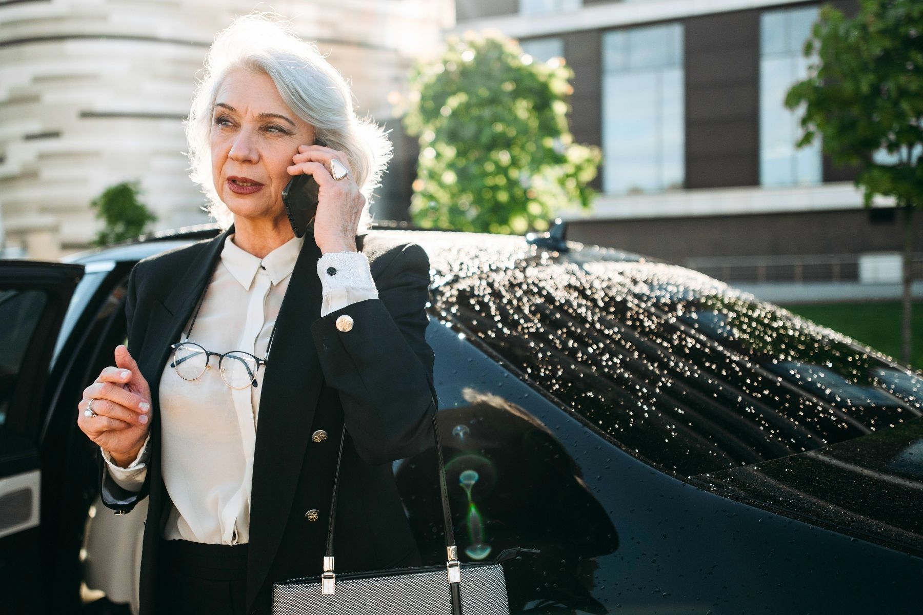 Senior businesswoman talking on phone next to a car
